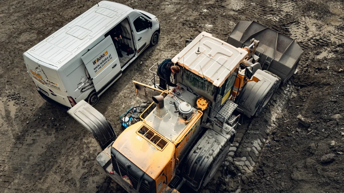 Mechanik WIBAKO serwisuje ładowarkę kołową w terenie, obok bus serwisowy z otwartymi drzwiami