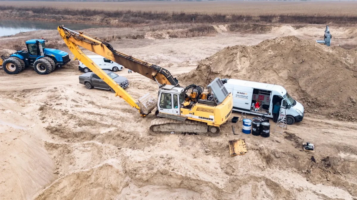 Koparka gąsienicowa Liebherr z długim ramieniem serwisowana w żwirowni obok busa serwisowego WIBAKO i beczek z olejem