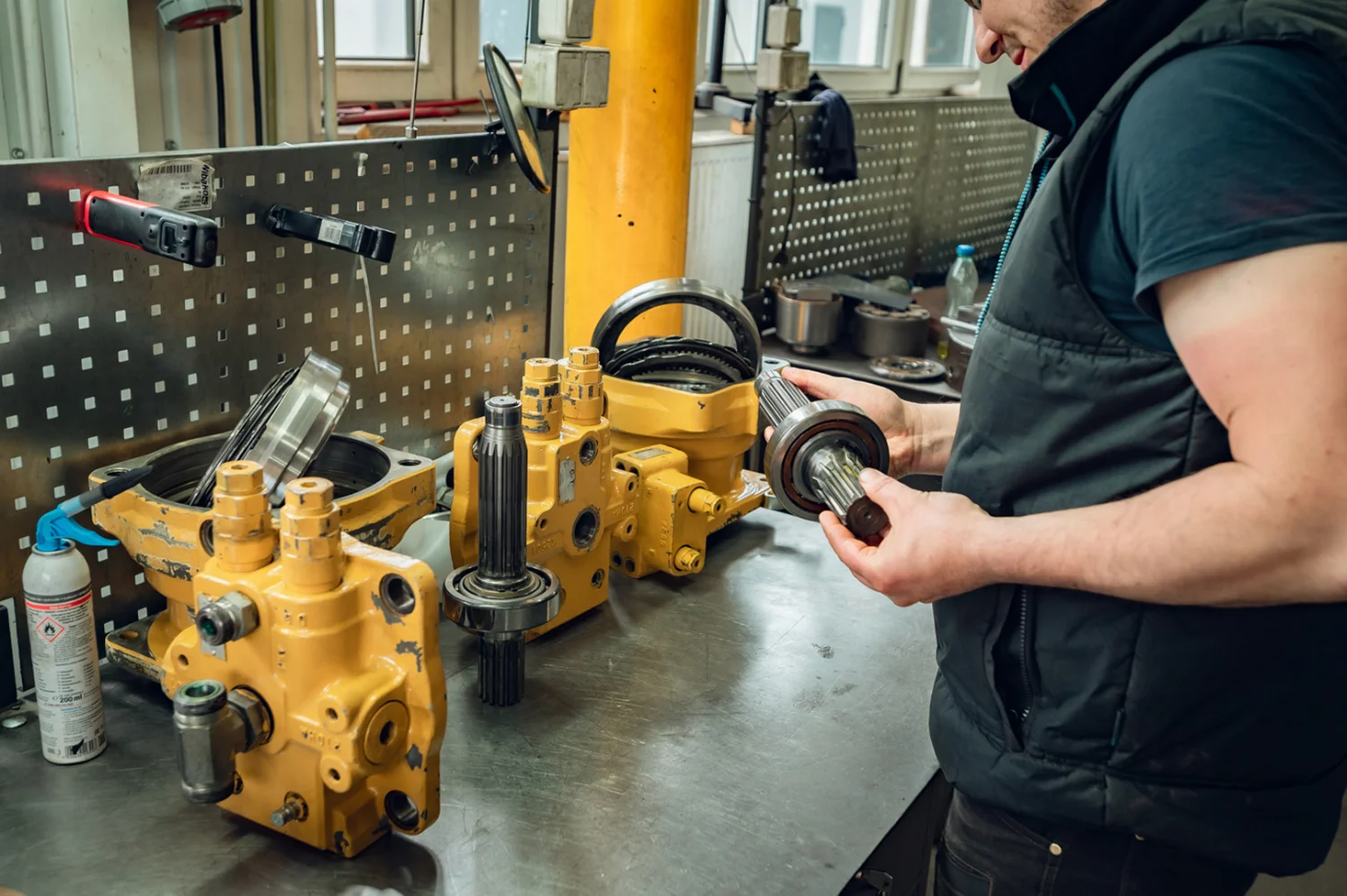 Mechanik ogląda wałek z łożyskiem przy rozebranym żółtym silniku hydraulicznym obrotu na stole