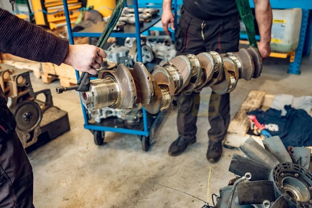 Mechanicy przenoszą wał korbowy silnika diesla na pasach transportowych w warsztacie regeneracji silników