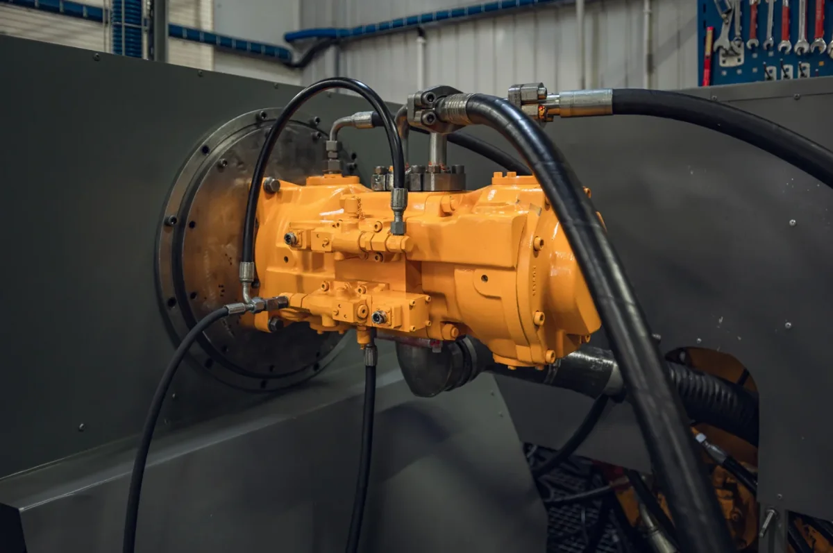 Żółta pompa tłoczkowa Liebherr po regeneracji podłączona przewodami hydraulicznymi do stanowiska testowego