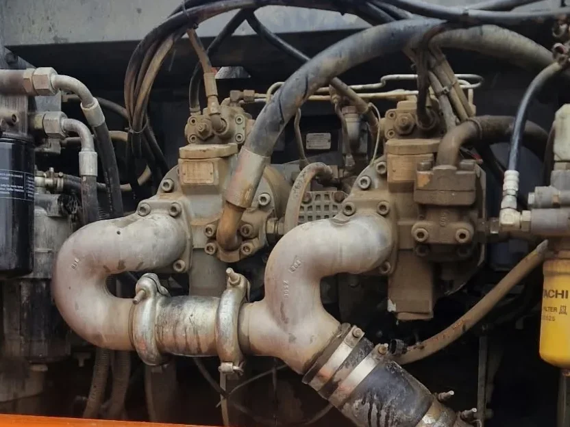Przedział pompy w Hitachi ZX350LC-3 z rurami ssawnymi pompy hydraulicznej, poniżej beczka na spuszczony olej